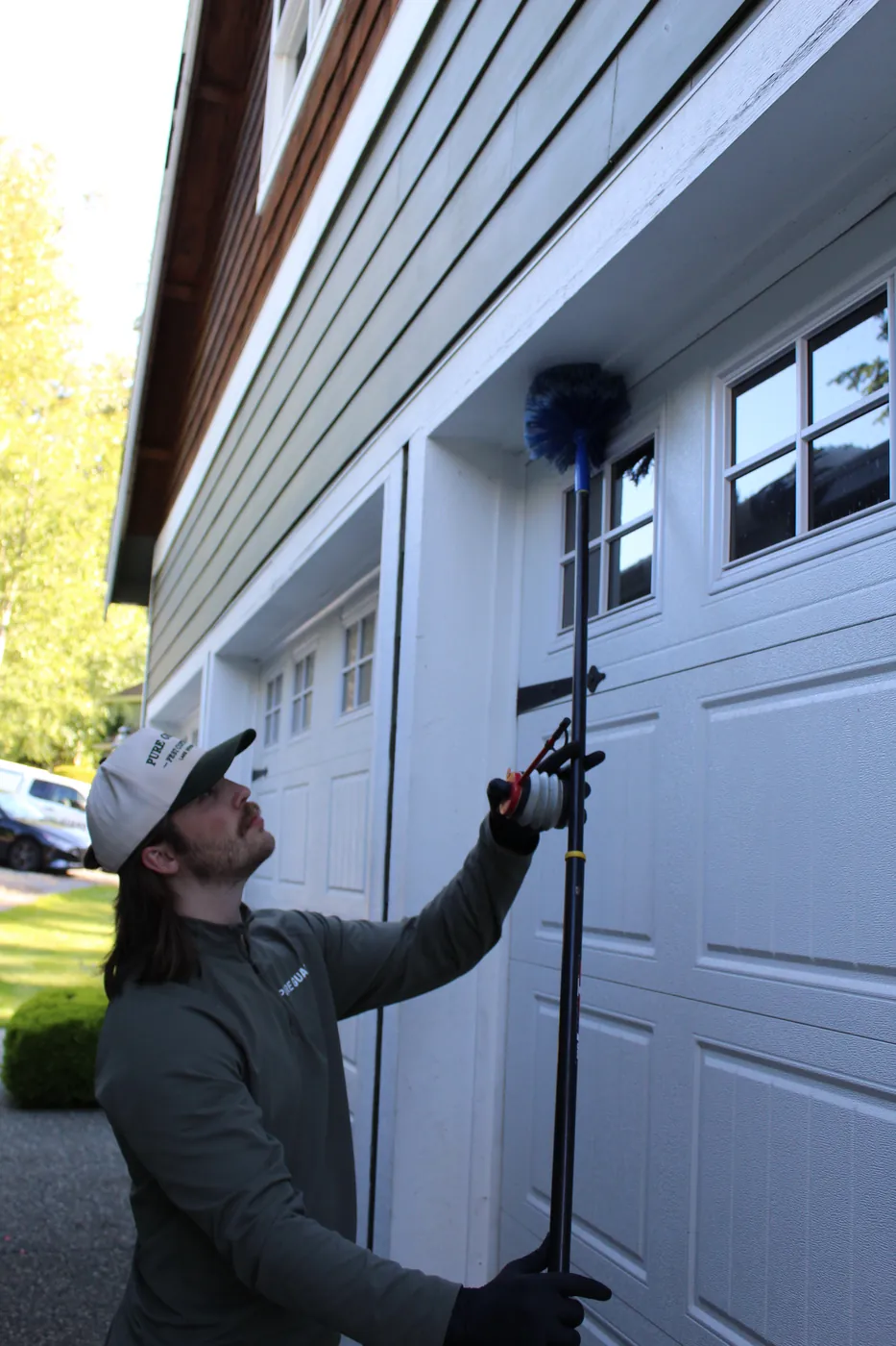Pure Guard technician in a branded pullover de-webbing the exterior of a home in Snohomish County, WA