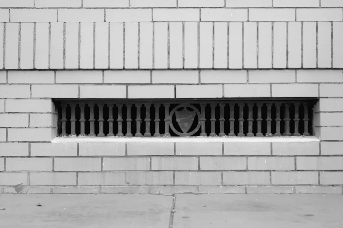 A black-and-white close-up of a long rectangular foundation vent with a decorative grille set into a brick wall