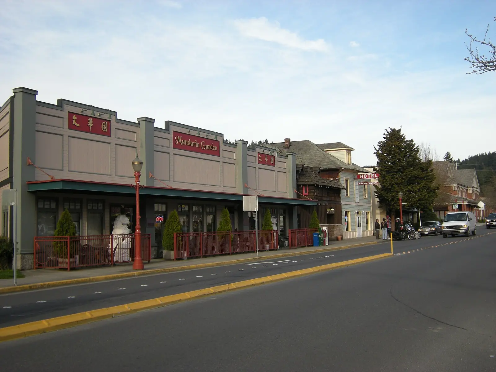 Older commercial buildings and a hotel sign along Sunset Way in Issaquah, WA, with forested hills rising behind the street