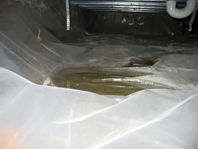 Water pooled on top of plastic sheeting on a crawl space floor, a sign the barrier is not keeping the space dry