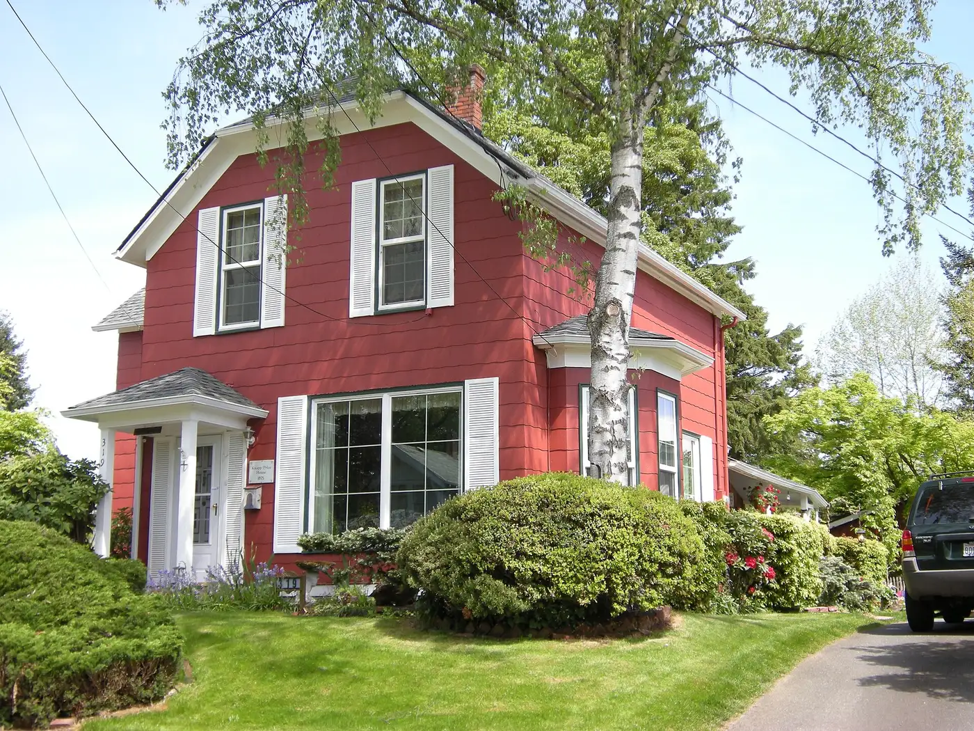 A red 1895 house on Avenue A in Snohomish, WA, with white shutters, a gambrel roofline, a bay window and a birch tree in the front yard