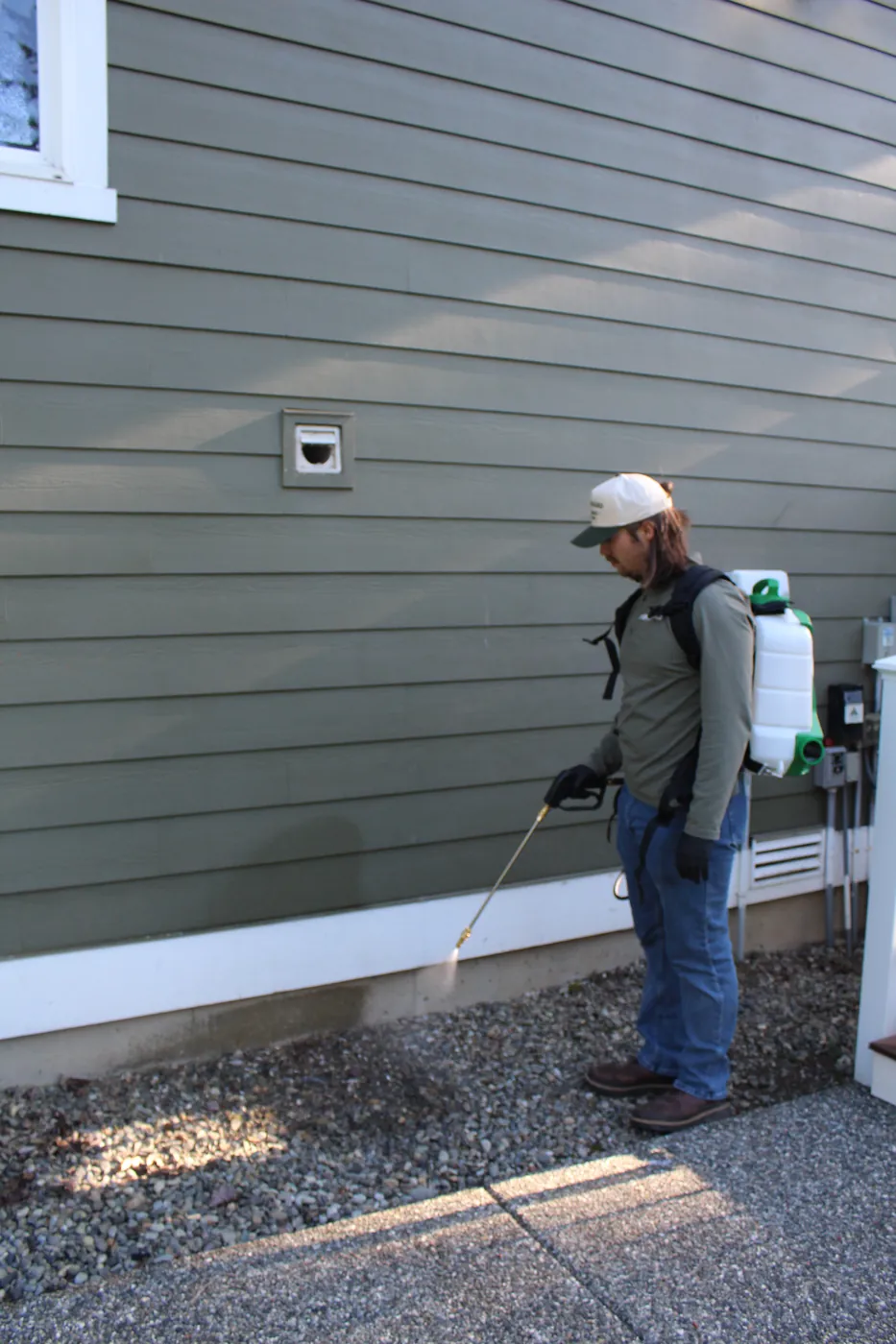 Pure Guard technician spraying a perimeter barrier along a home's foundation for ant control in Lake Stevens, WA