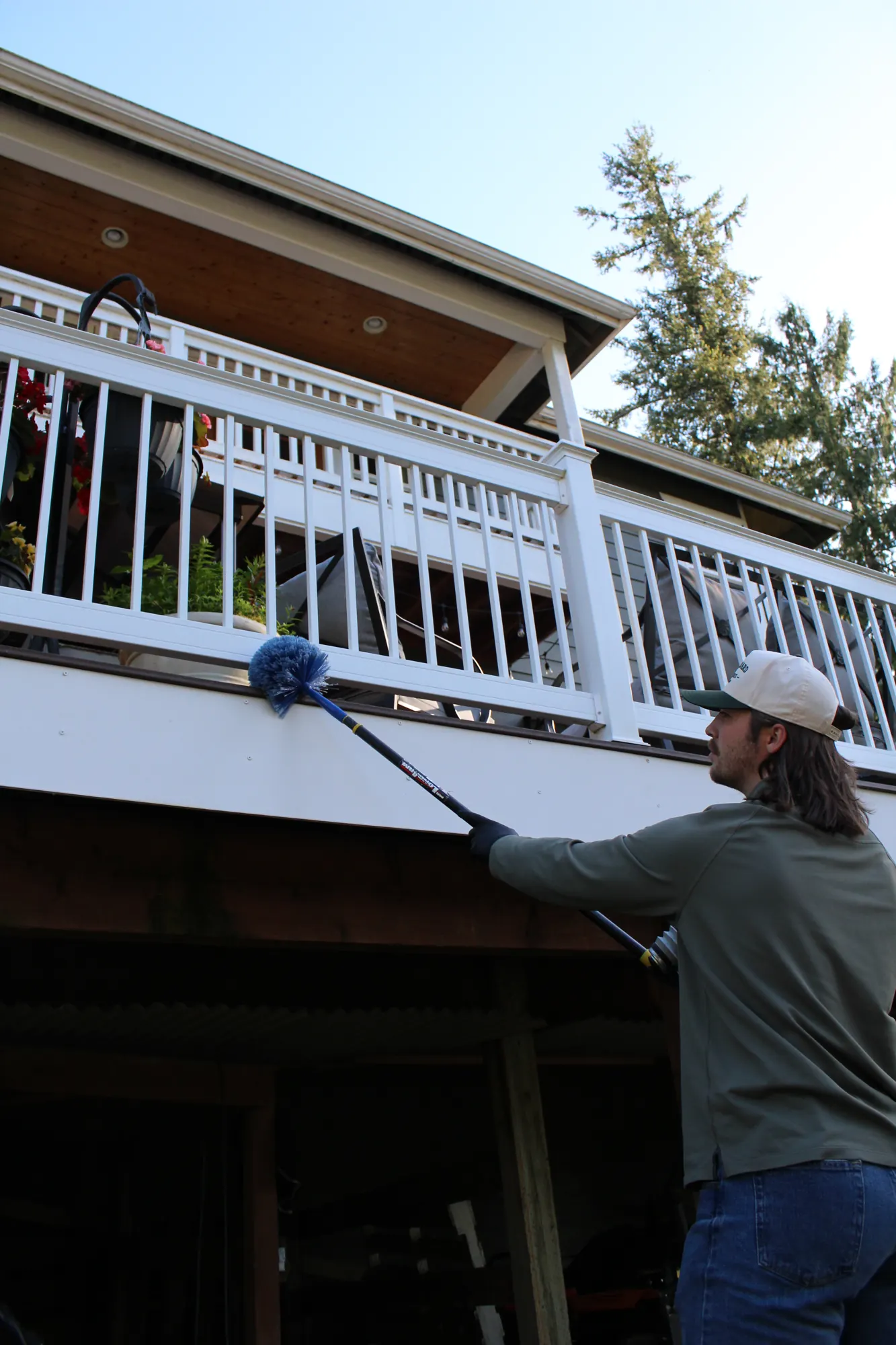 Pure Guard technician clearing nests and webs from under a deck rail on a wooded Woodinville, WA property