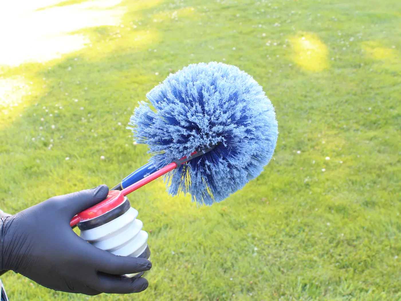 A gloved hand holding a Pure Guard extension web duster over a sunny green lawn