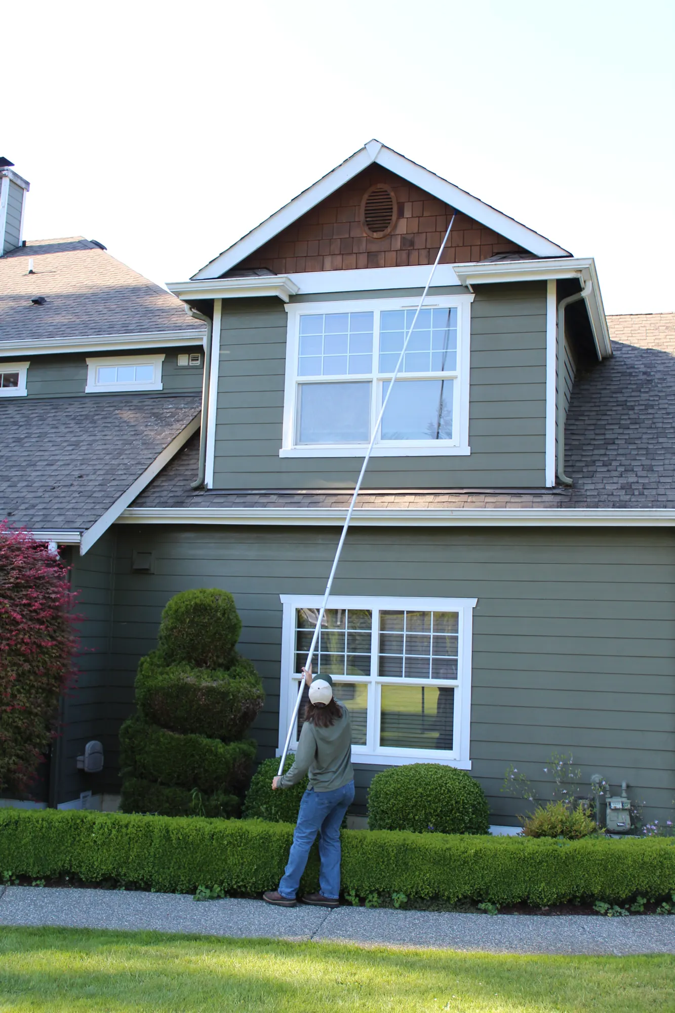 Pure Guard technician clearing webs from the upper eaves of a Lynnwood, WA home with an extension pole
