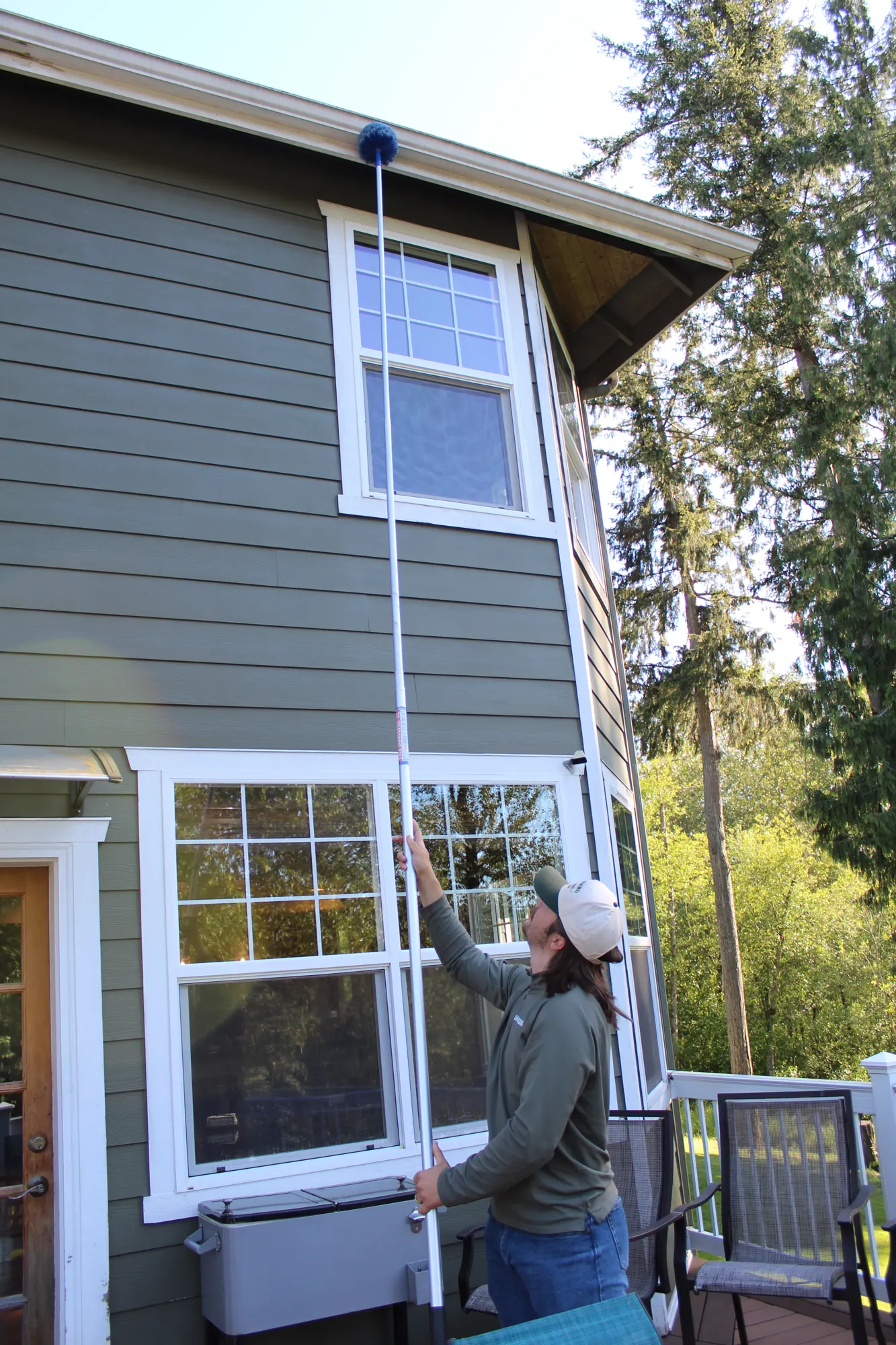 Pure Guard technician reaching a second-storey window and eave with an extension pole from a deck in Edmonds, WA