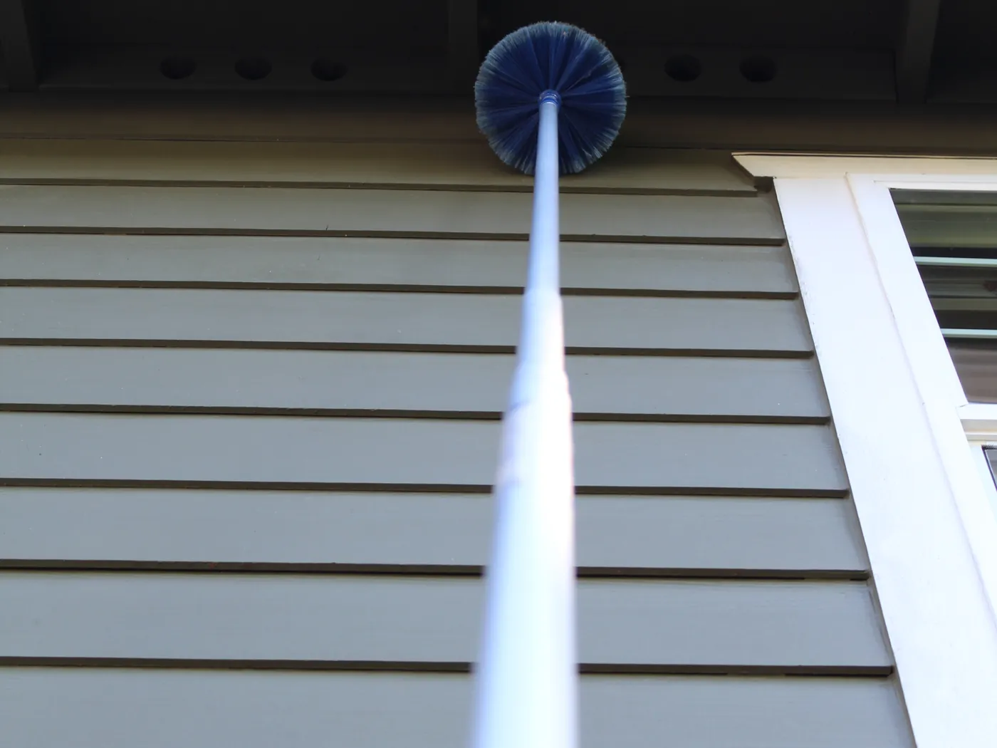 Pure Guard de-webbing a home's siding and eaves with an extension brush, Lake Stevens, WA